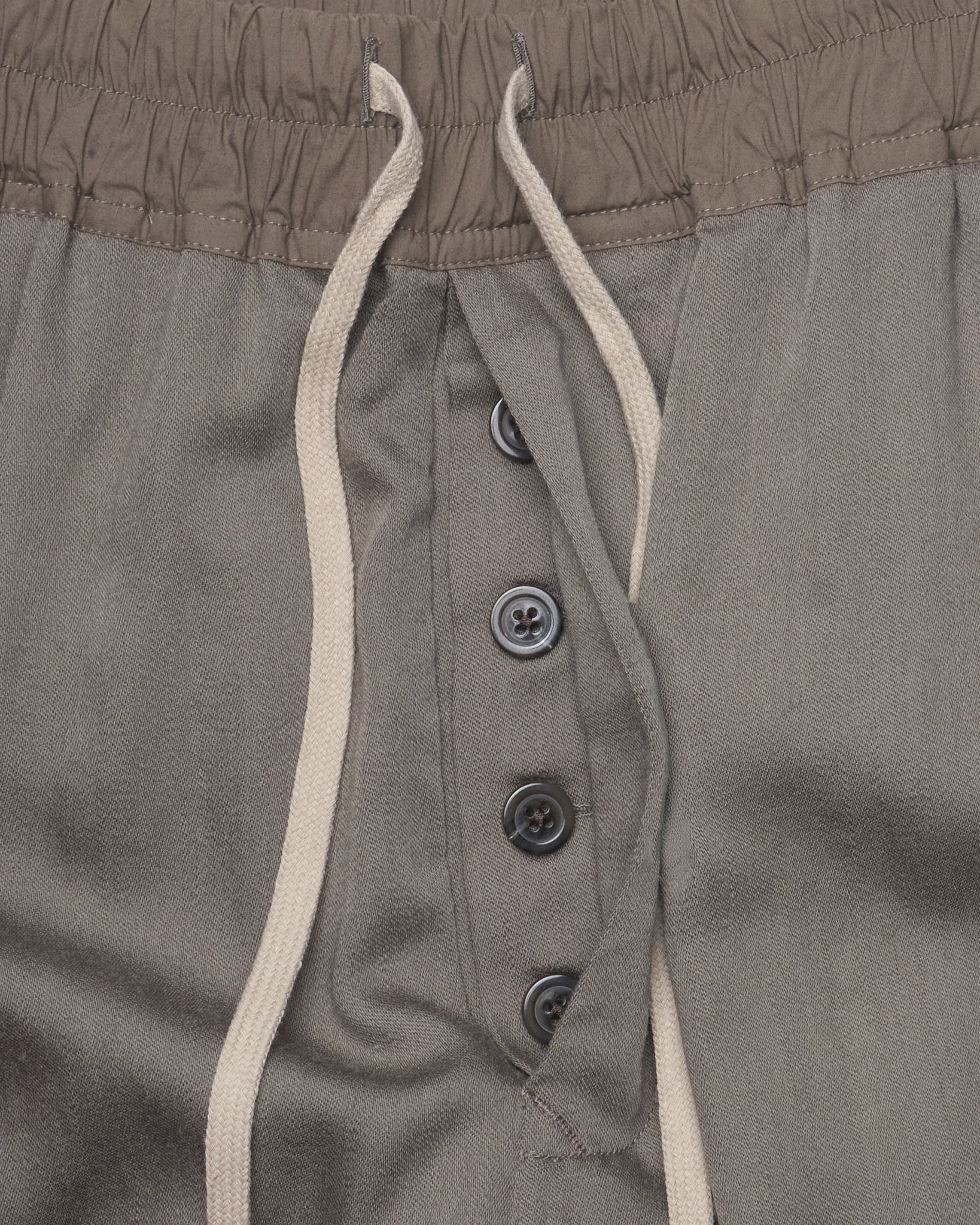 Close-up of brown pants with button details and white drawstring.