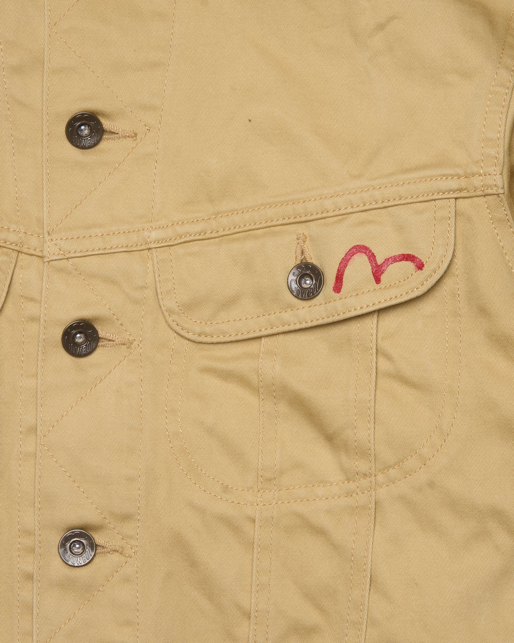 Close-up of a beige jacket with buttons and a pocket featuring a red heart design.