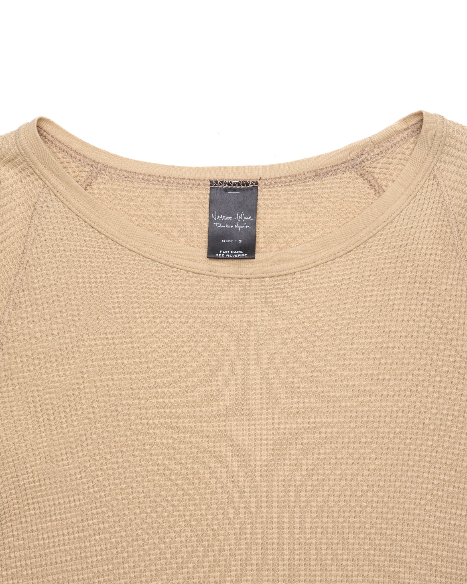 Close-up of a beige textured shirt with a brand label on a white background