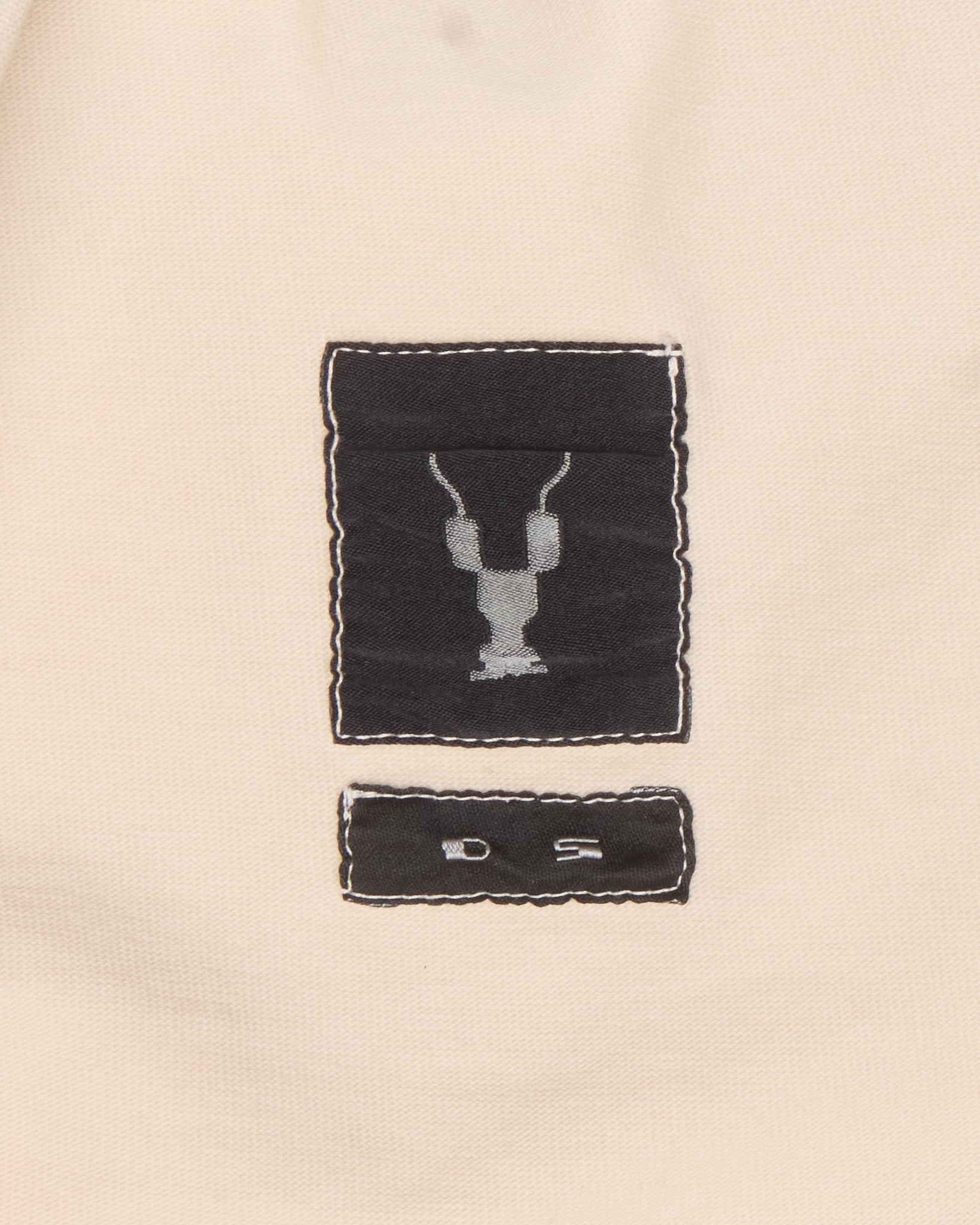 Close-up of a beige fabric with embroidered black labels featuring a design.