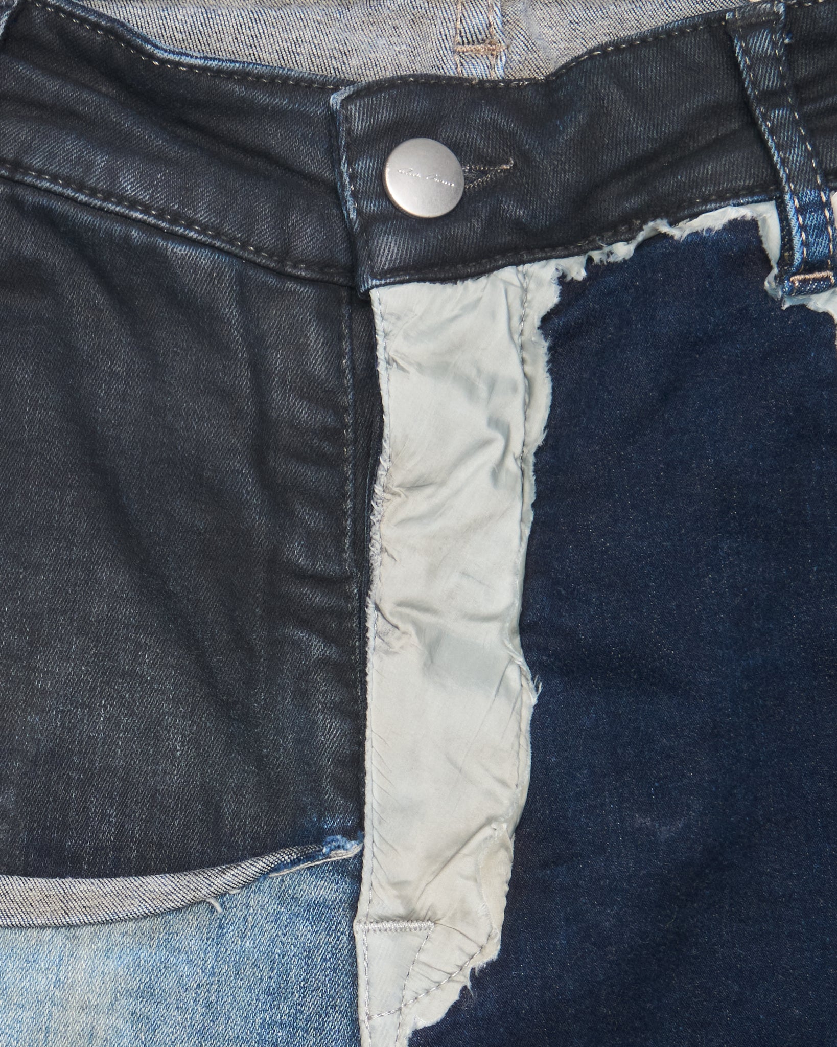 Close-up of a blue denim fabric with a button and frayed edge.