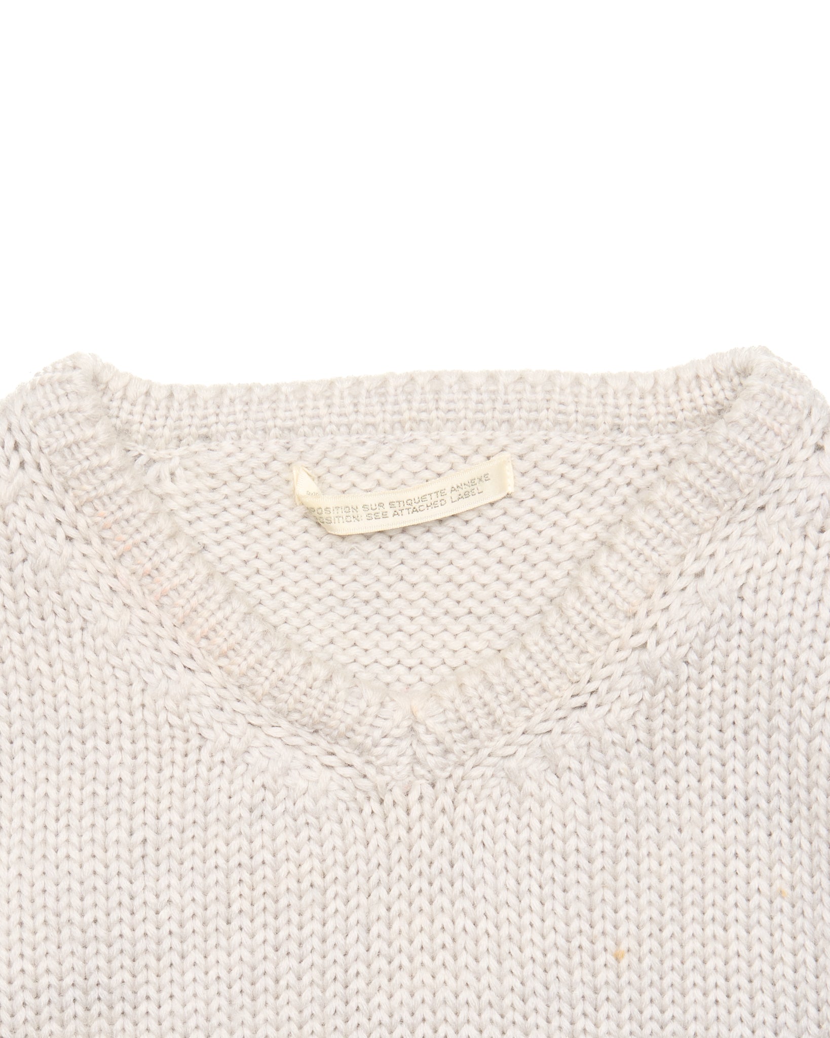 Close-up of a light gray knit sweater with a brand label on a white background